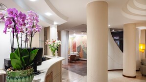 A reception area with a desk, a vase of orchids, and a modern interior design. - Hotel Carlo Felice (Sassari)