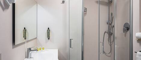 Un baño moderno con ducha de vidrio, lavabo blanco y un espejo grande.
