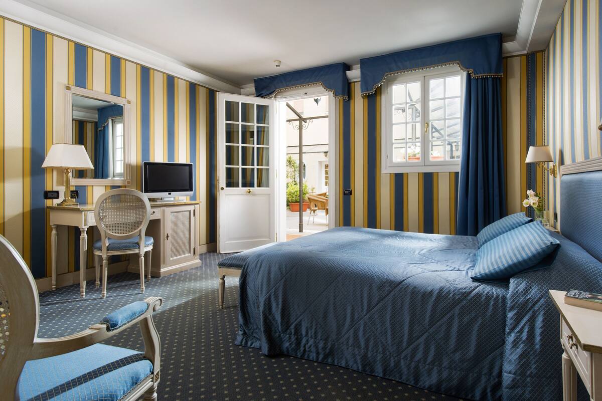 A hotel room with a bed, a desk with a computer, a chair, and a window with curtains.