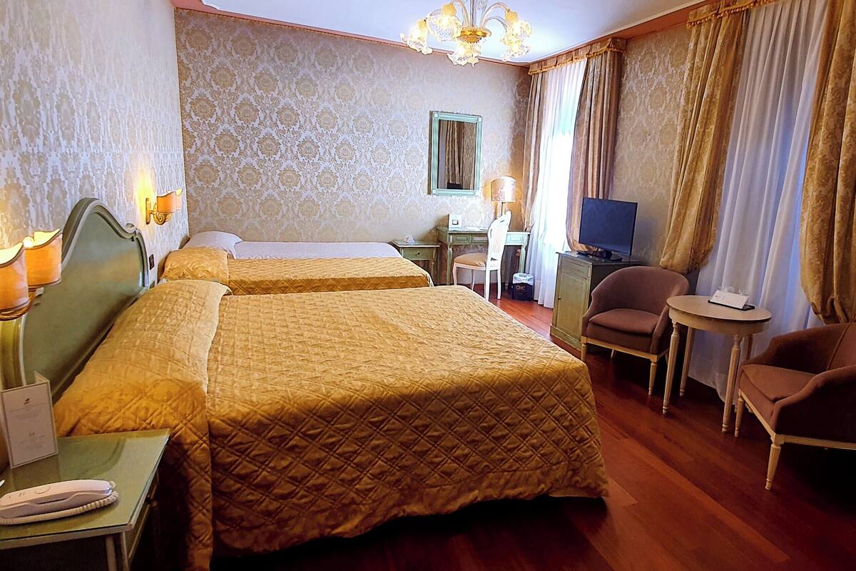 A hotel room with two beds, a desk, a chair, a television, and a small table.