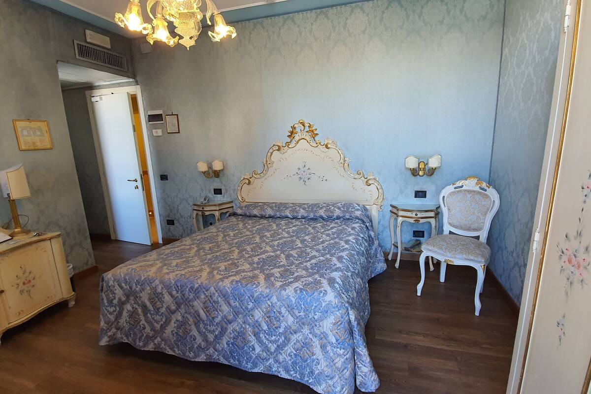 A bedroom with a large bed, a nightstand, a chair, and a desk.