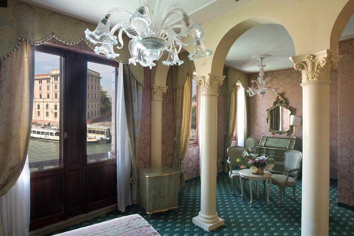 A hotel room with a large window, ornate chandelier, and classic furniture.