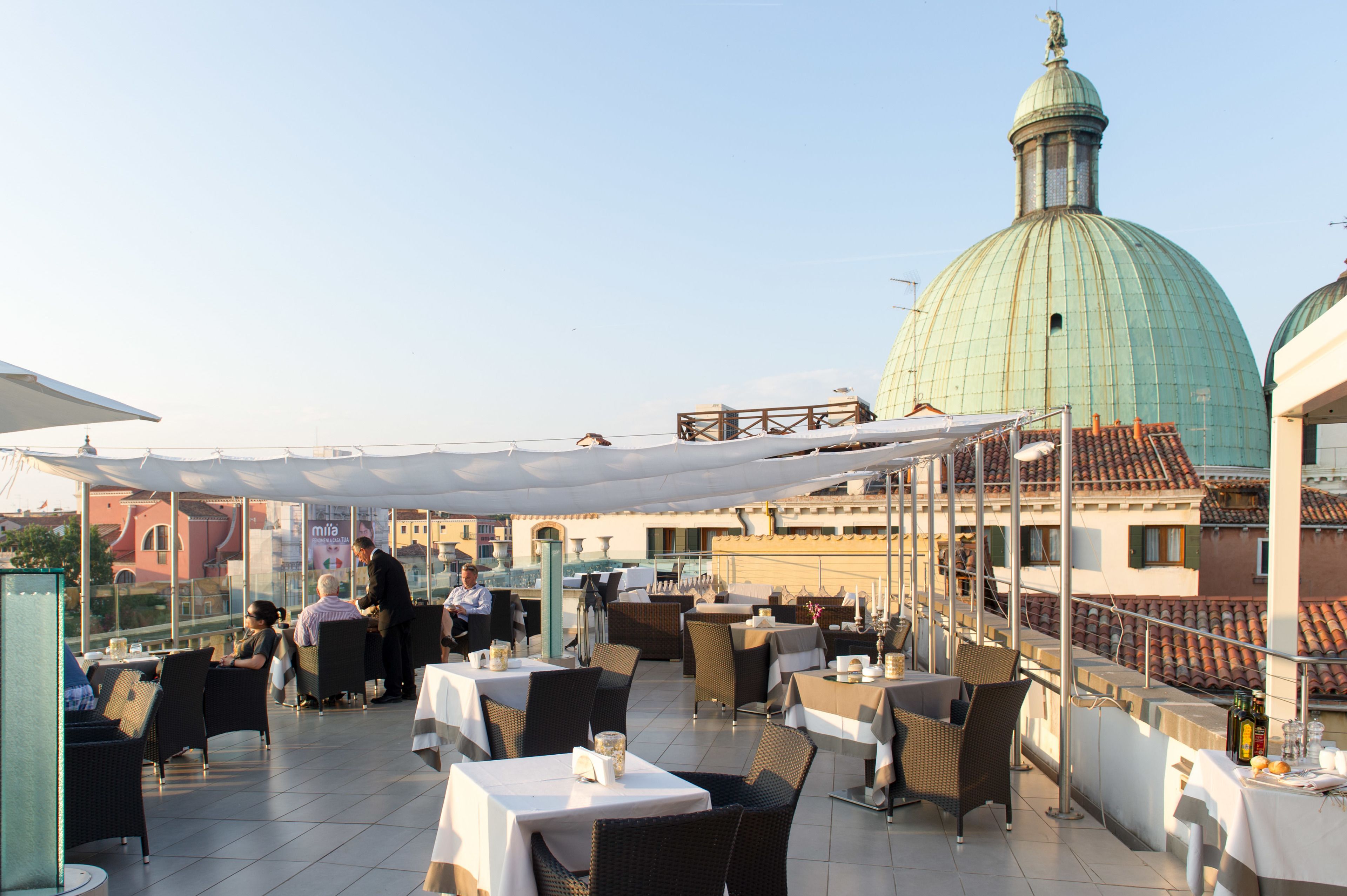 Un espace extérieur aménagé pour les repas, avec des tables et des chaises, une grande structure en forme de dôme en arrière-plan et un ciel dégagé.