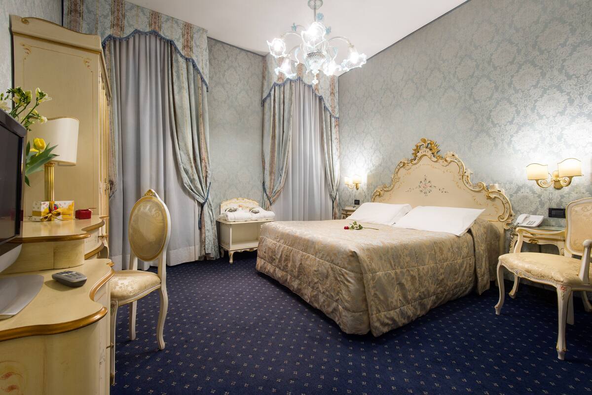 A hotel room with a large bed, a desk with a lamp, a chair, a dresser, and a mirror.