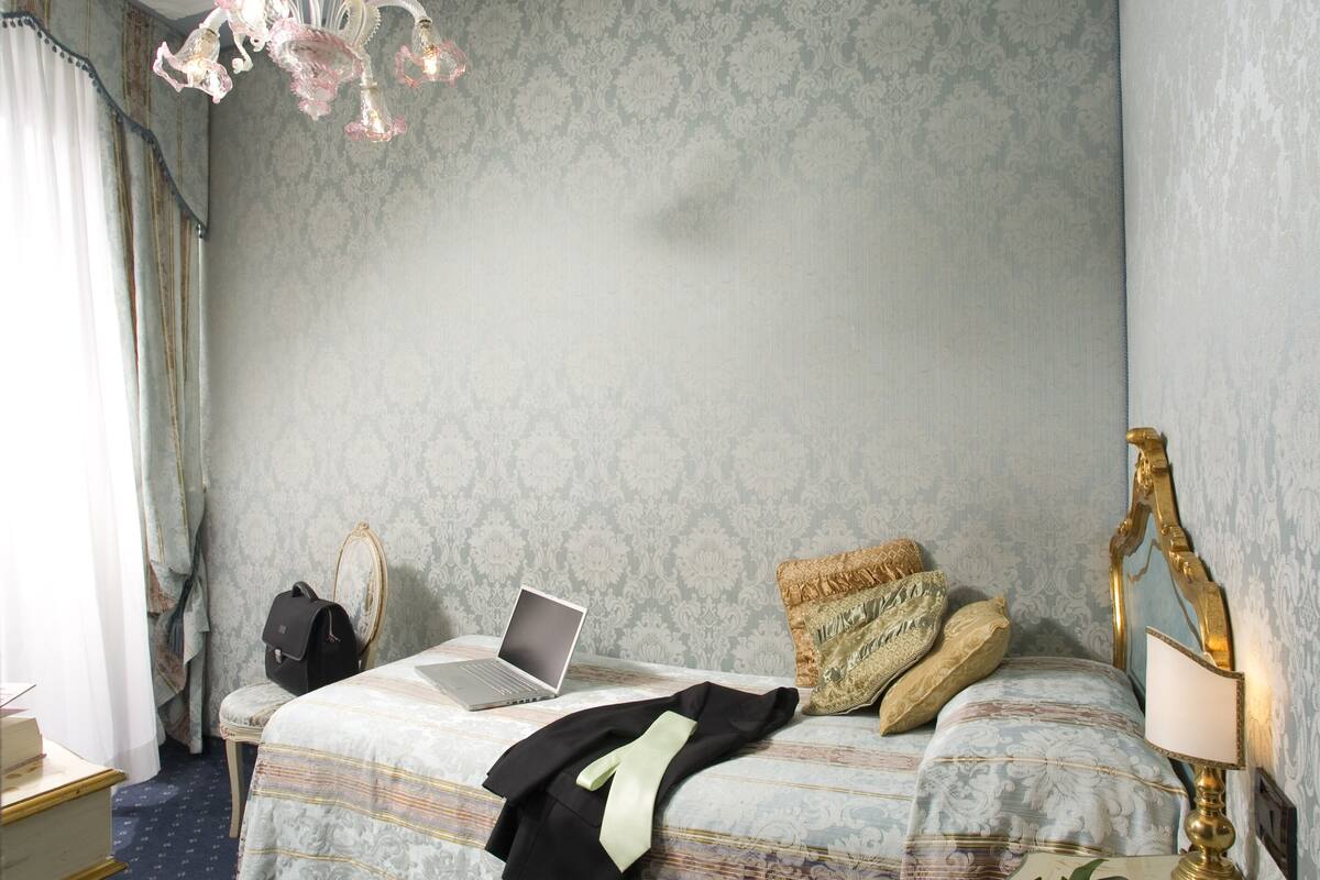 A bedroom with a bed, a laptop, a suitcase, a pair of shoes, a lamp, and a dresser.