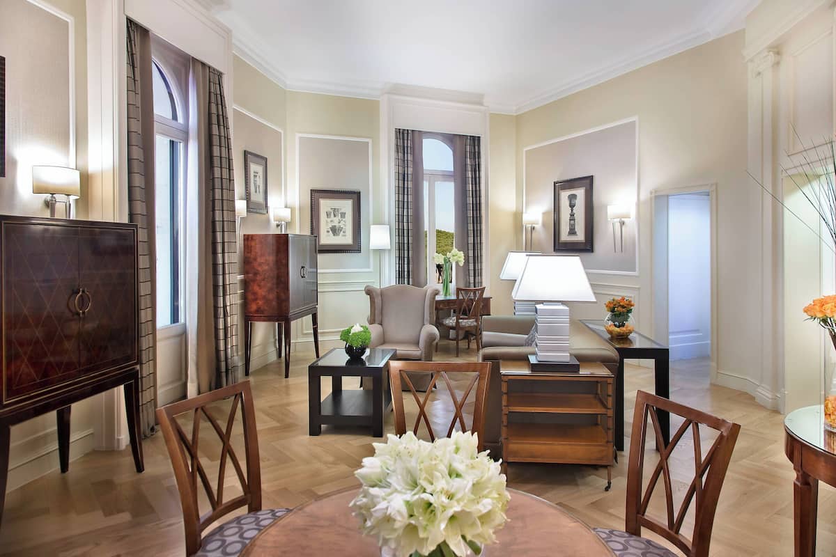 A spacious living room with a wooden coffee table, a sofa, and a TV stand. There are two side tables with lamps and a vase with flowers on one of them.