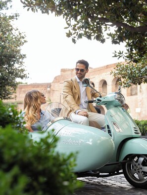 A vintage scooter with 'Rome on sidecar' written on it, a man in a beige suit, and a woman in a blue shirt.