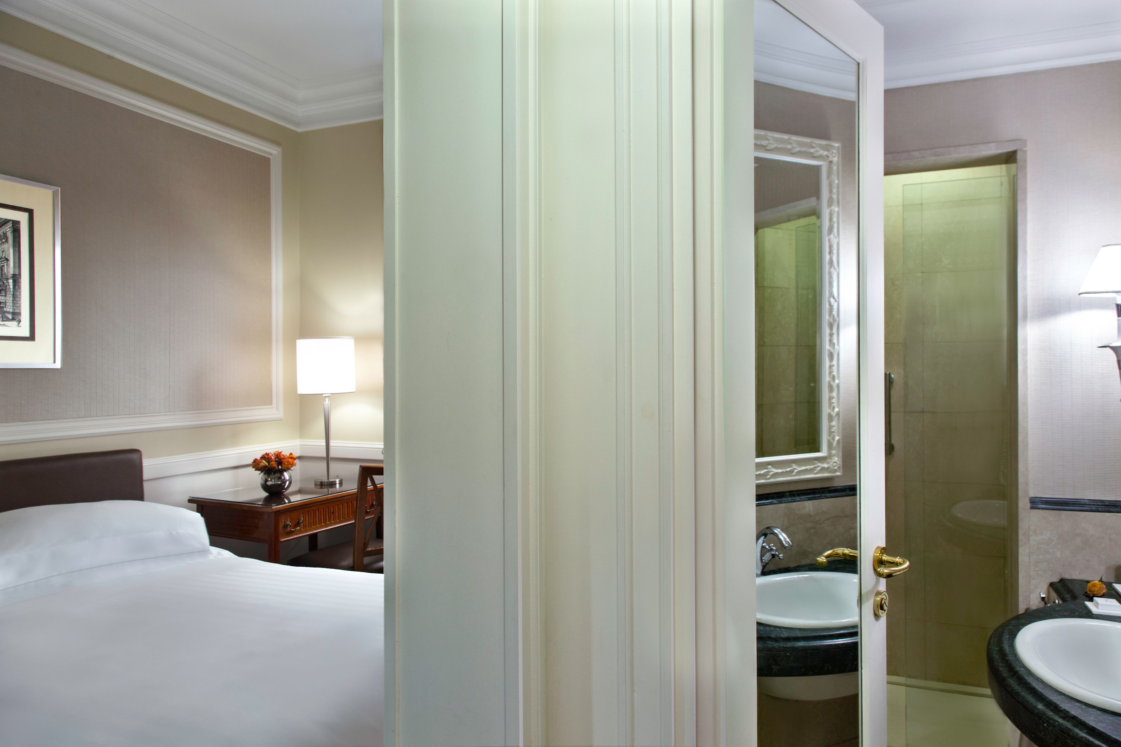 A hotel room with a bed, a nightstand with a lamp, a bathroom with a sink and mirror.