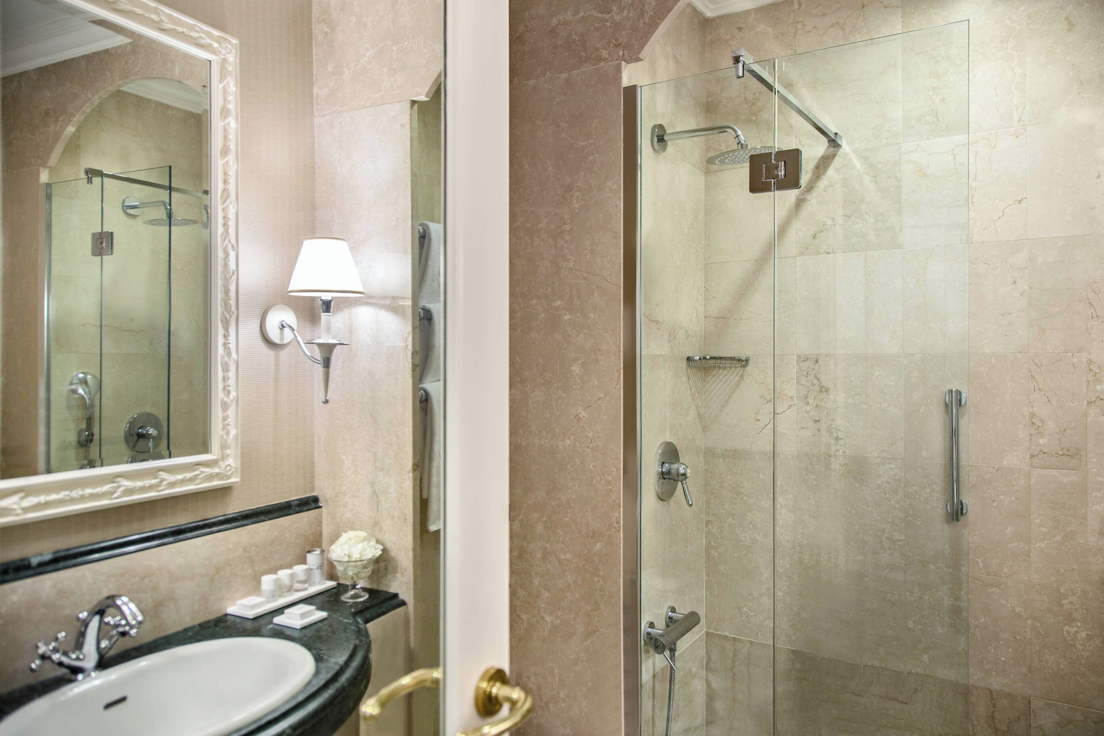 A bathroom with a marble sink, a glass-enclosed shower, and a wall-mounted mirror.