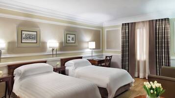 A hotel room with two beds, a desk, a chair, a lamp, and a vase of flowers.