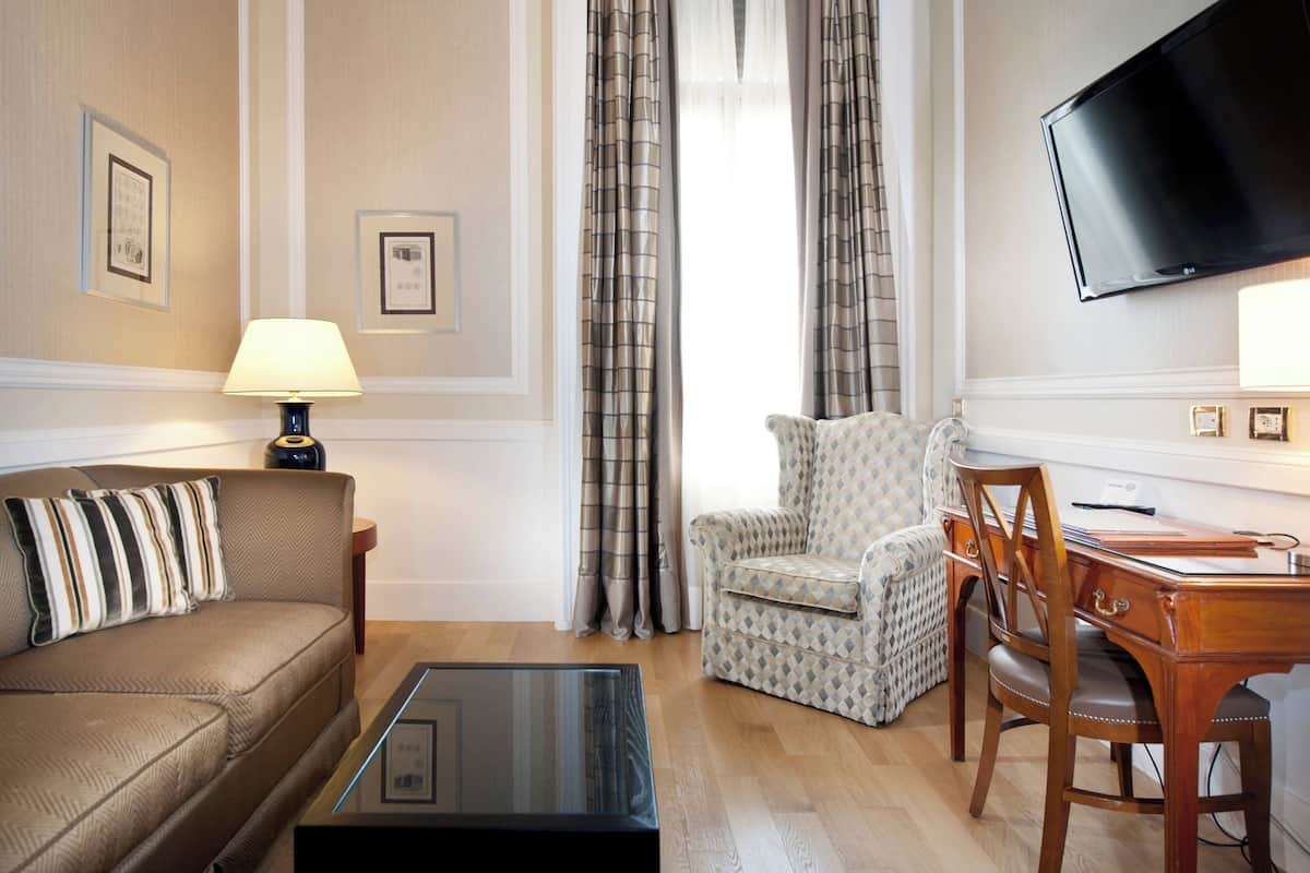 A living room with a sofa, armchair, and a TV mounted on the wall.