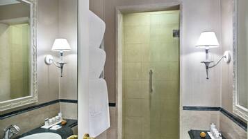 A bathroom with a sink, mirror, towel rack, shower, and two wall-mounted lamps.