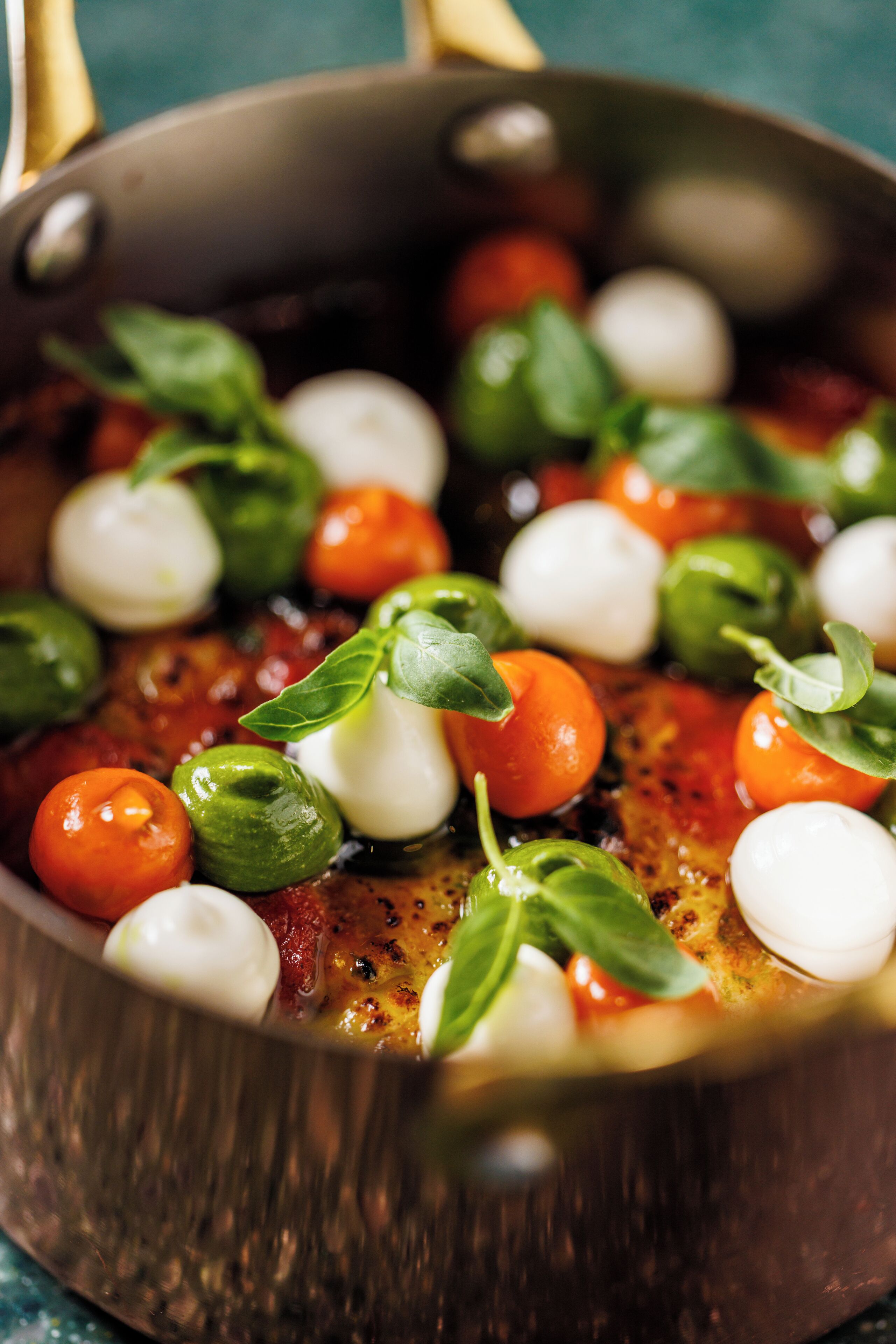 A close-up of a cooking pan with tomatoes, mozzarella, and basil.