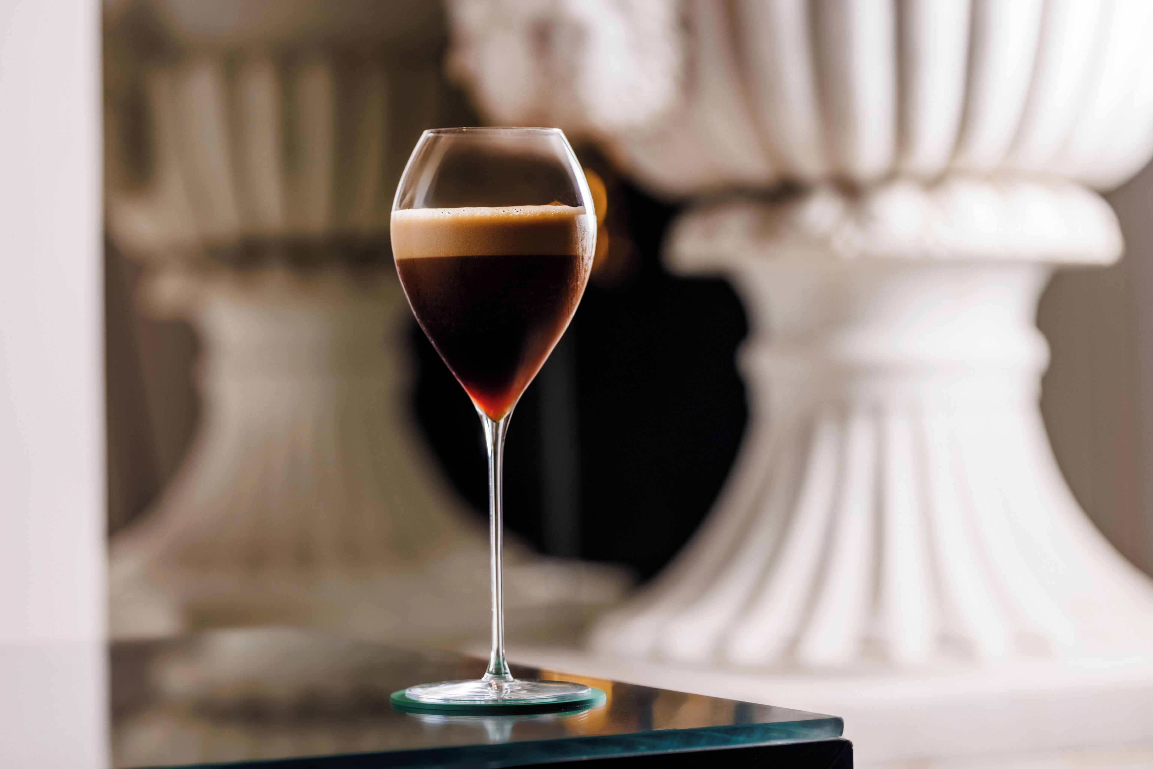 A glass of dark liquid on a glass coaster.