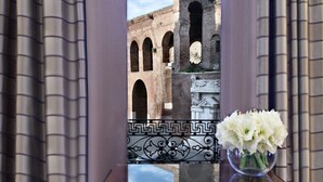 Un balcon offrant une vue sur un ancien bâtiment en briques, doté d’arcades, d’une balustrade décorative et d’un vase rempli de fleurs.