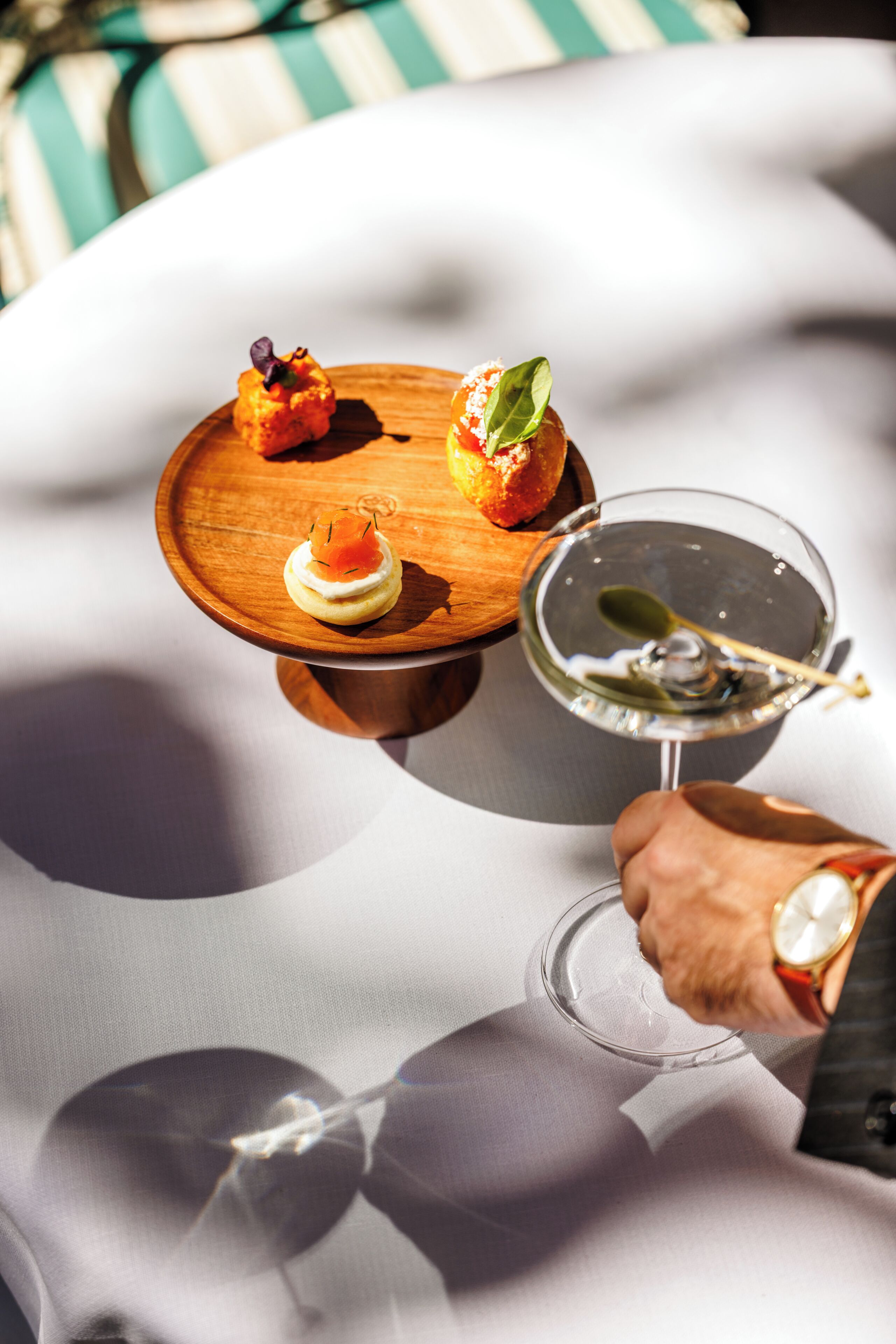 A table with a wooden board holding three appetizers and a martini glass.