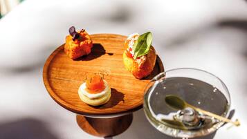 A table with a wooden board holding three appetizers and a martini glass.