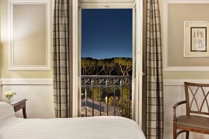 A hotel room with a bed, a chair, a nightstand, and a view of a balcony with a railing.