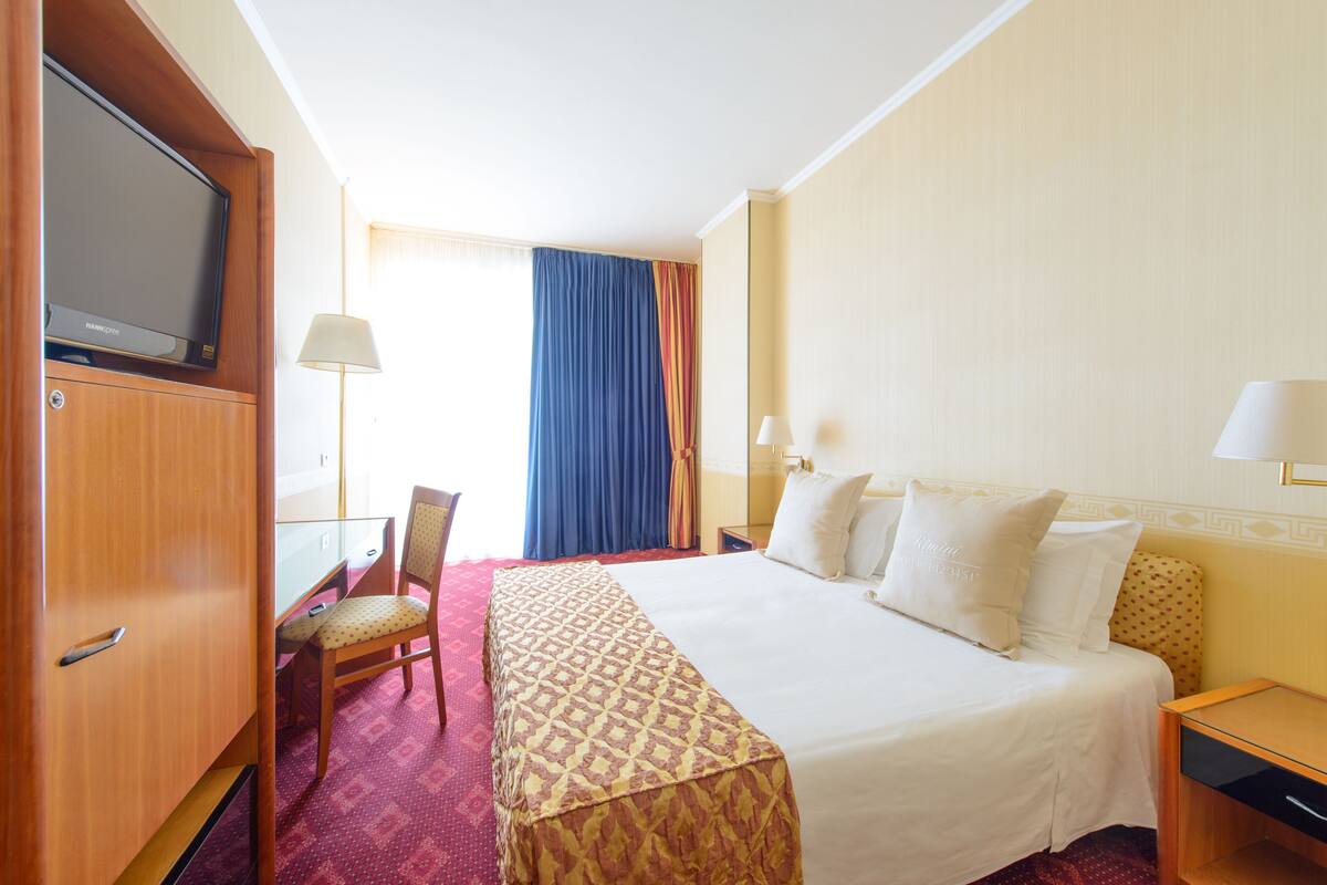 A hotel room with a bed, a desk with a computer, a TV, and a chair.