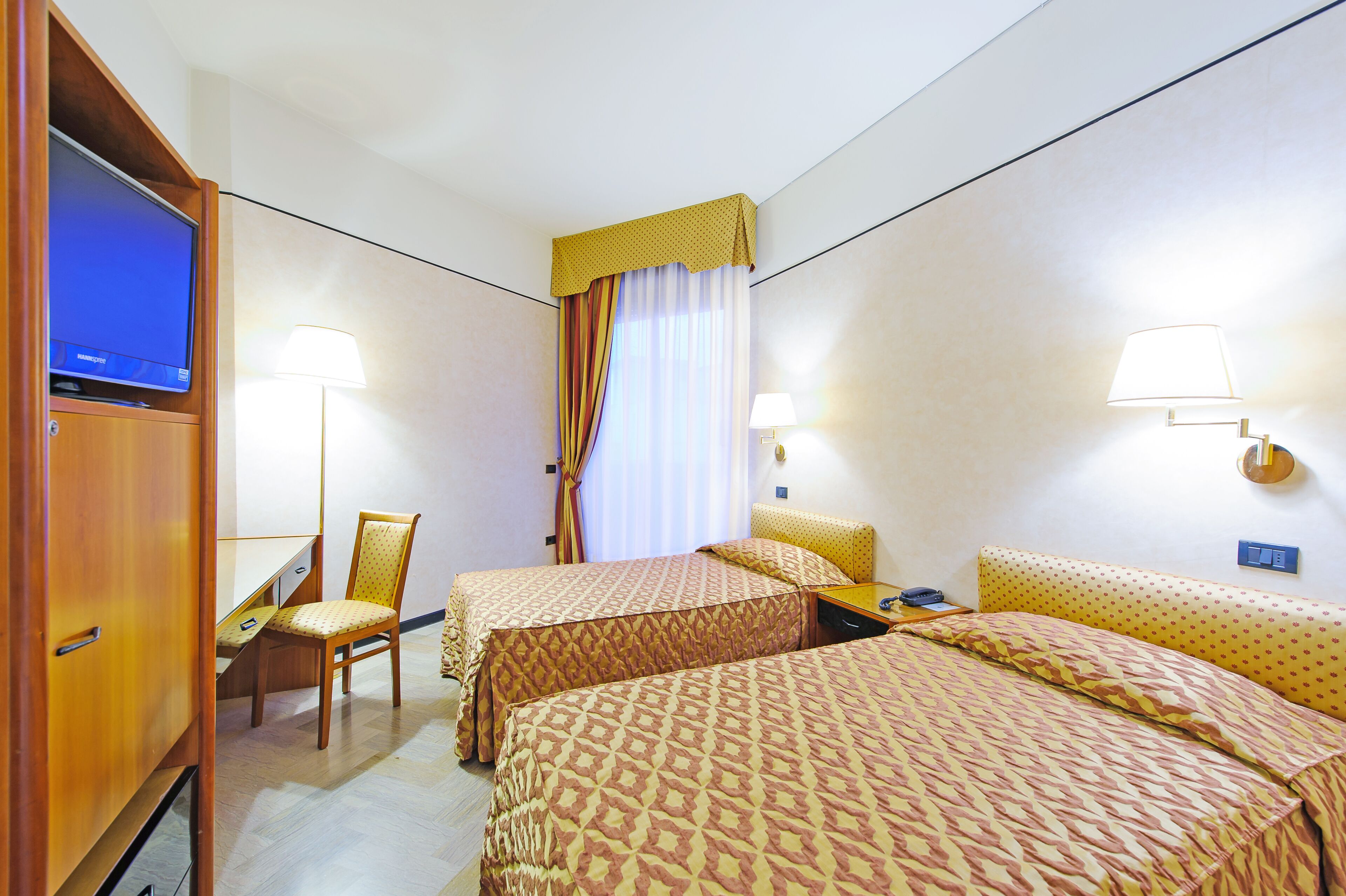 A hotel room with two beds, a desk, a chair, a television, and two bedside lamps.