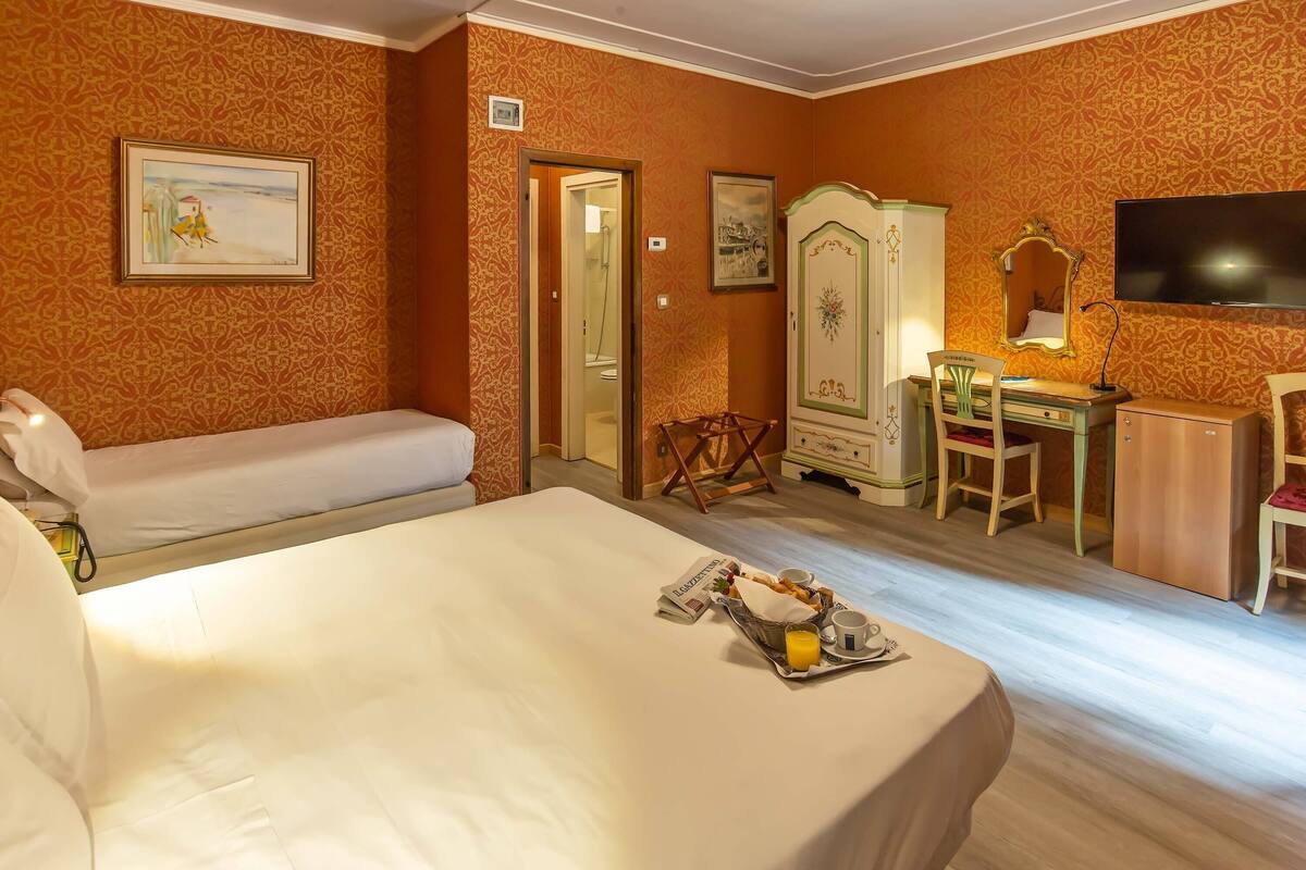 A hotel room with a bed, a desk, a chair, a wardrobe, and a television.