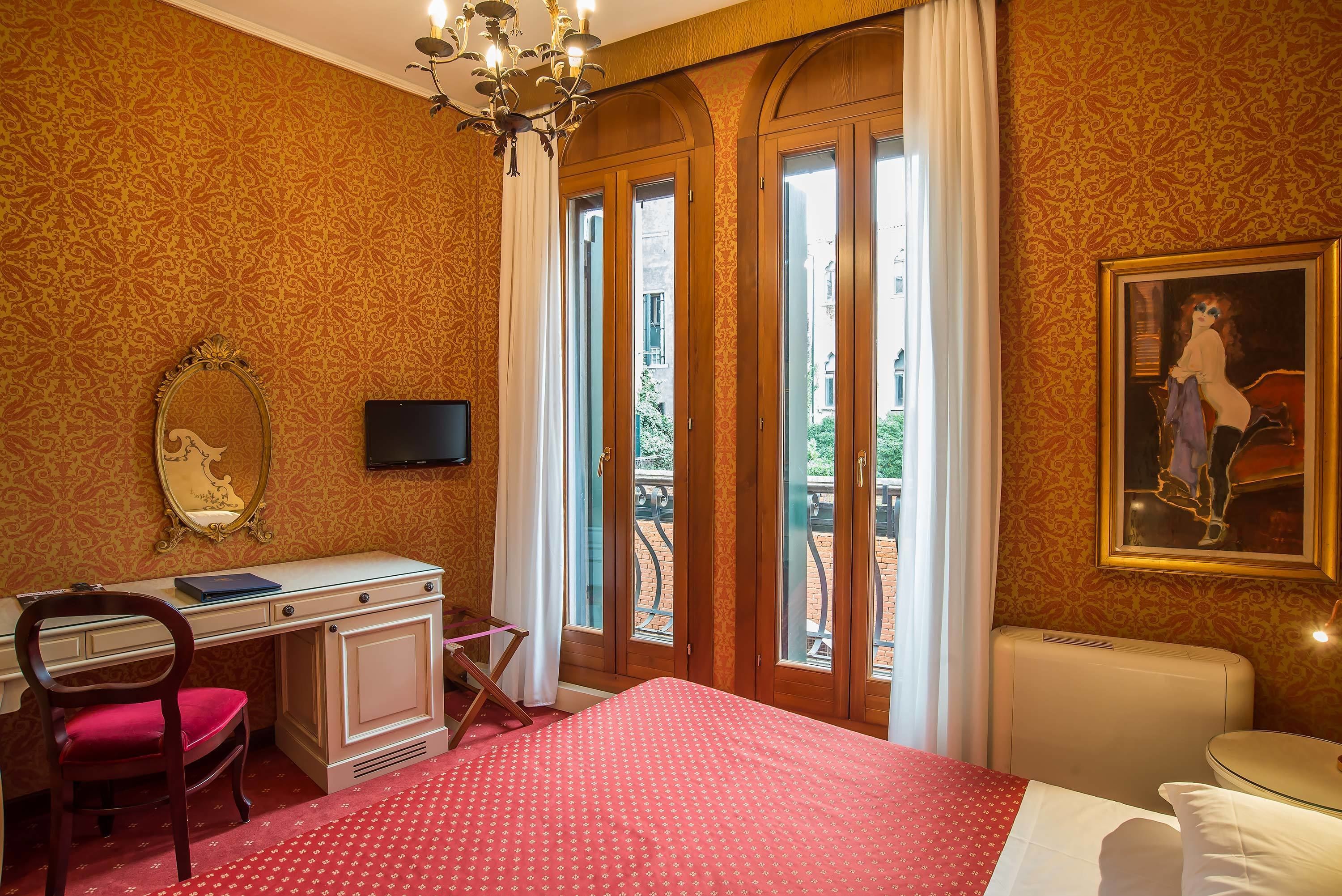 Habitación de hotel con cama, escritorio, silla, televisión y ventana con vista al exterior.