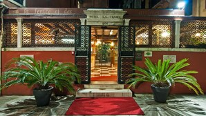 De ingang van Hotel La Fenice met een zwart-witte vloer, potplanten en een rode loper.
