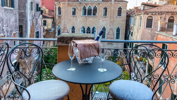 Een balkon met een ronde tafel, twee stoelen en twee glaasjes water.