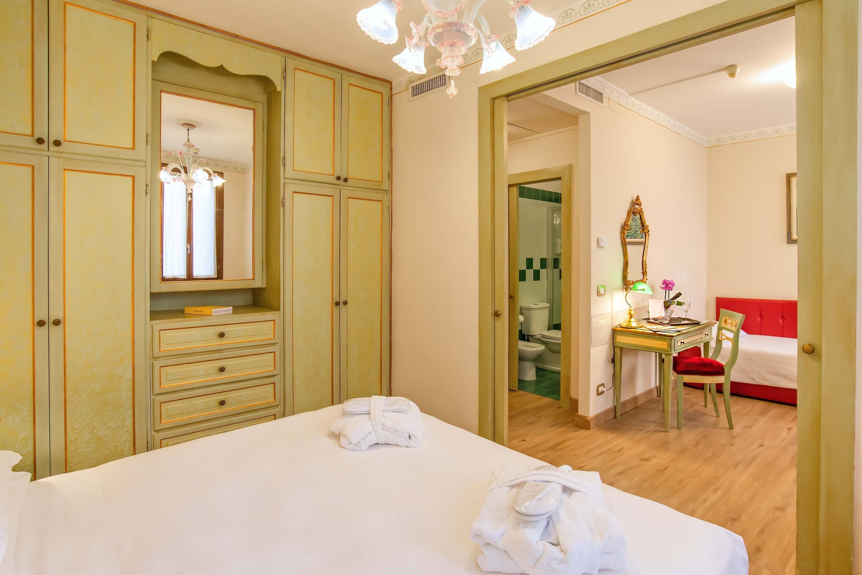 Habitación de hotel con una cama grande, un escritorio con silla, un espejo y una colcha roja.