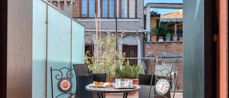 Une cour avec une table ronde et quatre chaises, entourée de plantes en pot et d’un bâtiment doté de fenêtres en arc de cercle.