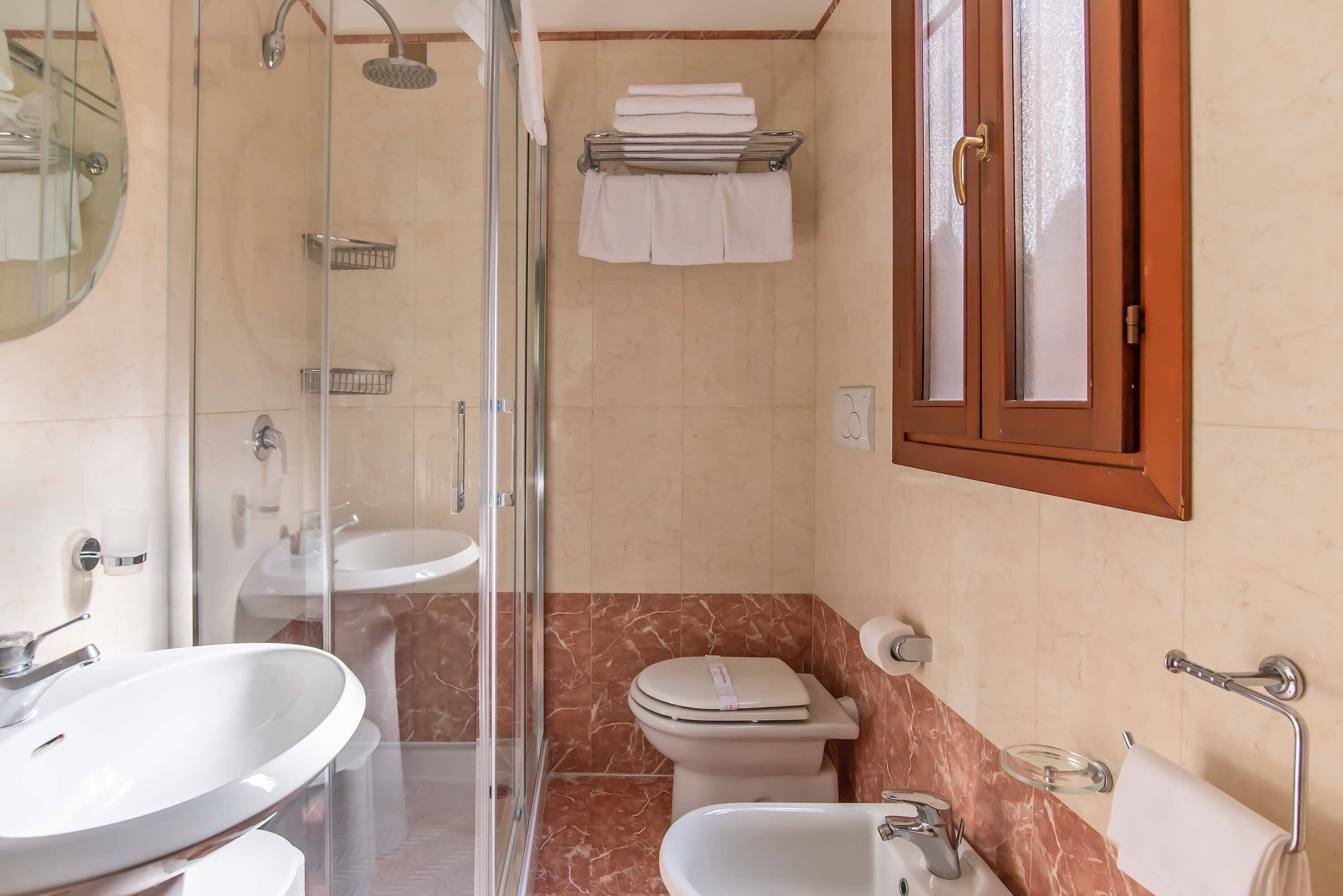 A bathroom with a glass-enclosed shower, a sink, a toilet, and a bathtub.