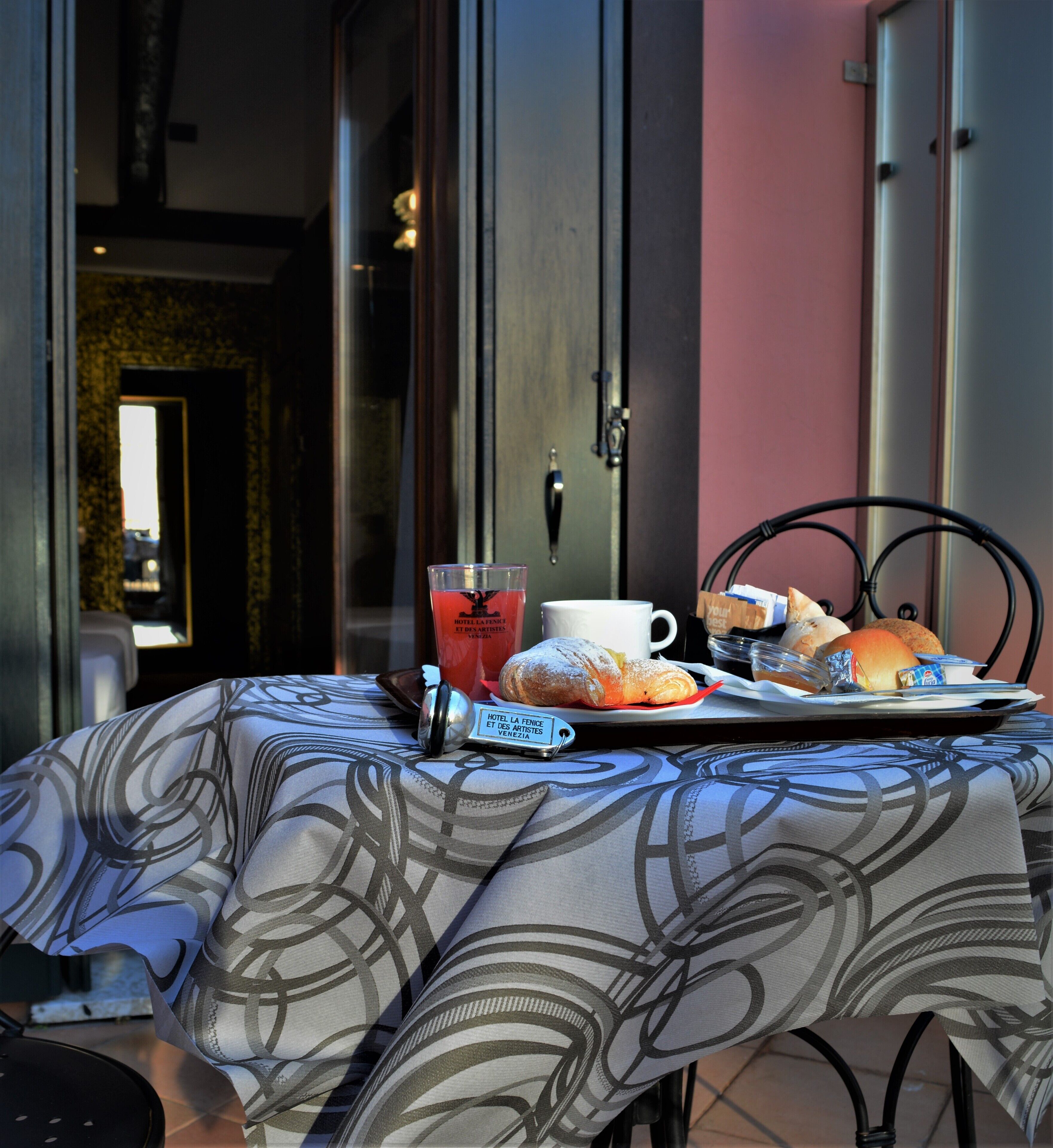 A breakfast tray with croissants, a muffin, and a beverage on a table with a patterned tablecloth.