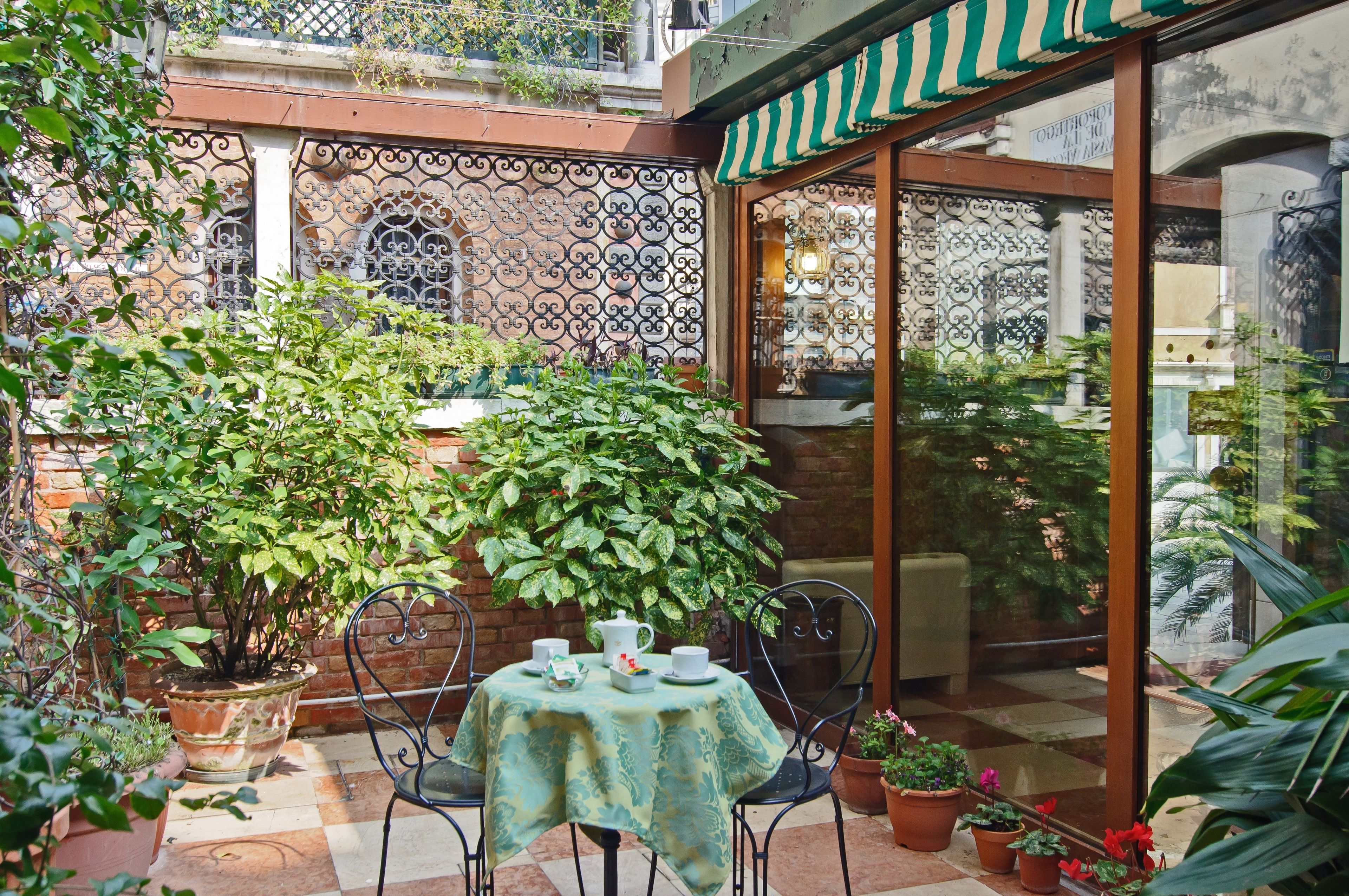 A patio with a table set for two, surrounded by potted plants and a decorative fence.