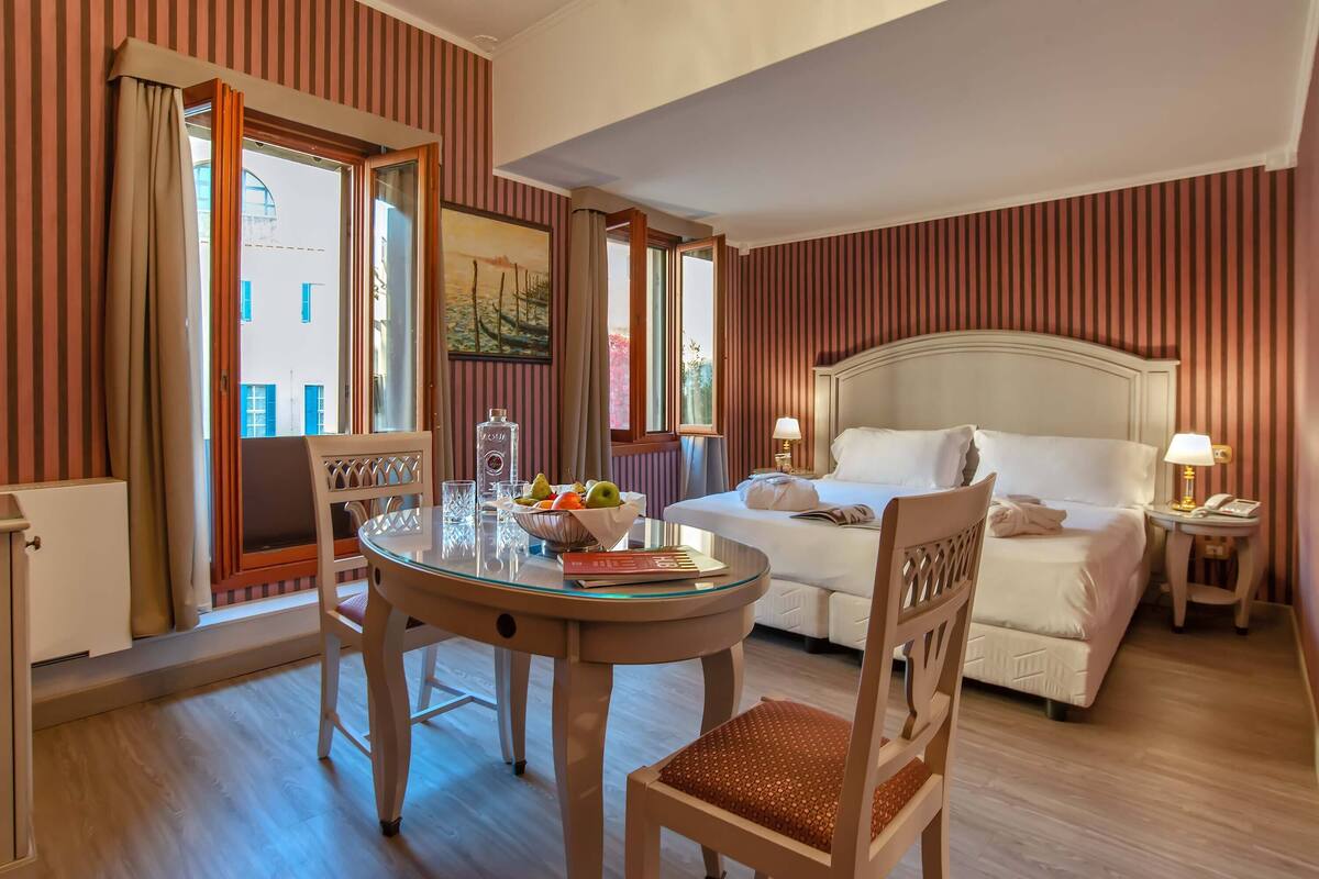 Une chambre d’hôtel comprenant un lit, une table de chevet, une lampe et un coin repas avec une table et des chaises.