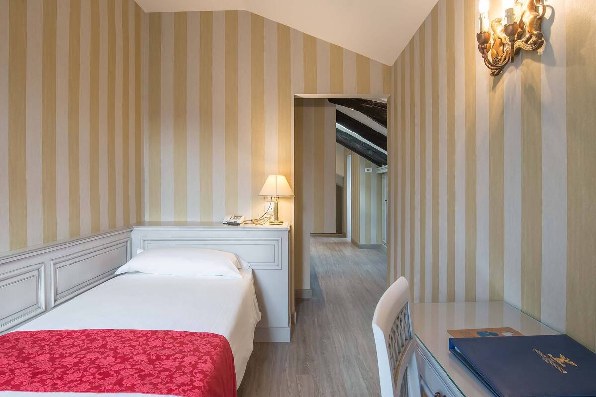Une chambre d’hôtel avec un lit, une table de chevet avec une lampe, une chaise et un bureau avec un livre.