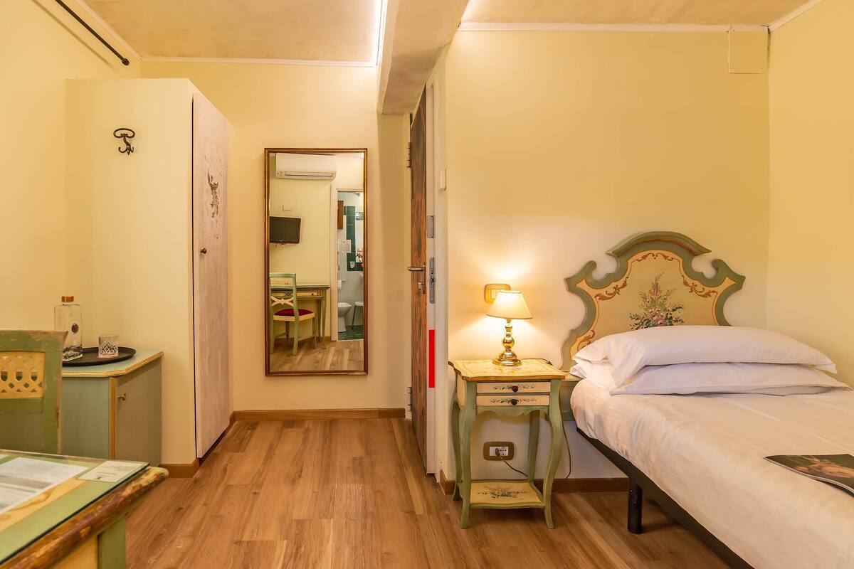 A bedroom with a bed, a bedside table with a lamp, a mirror, and a small cabinet.