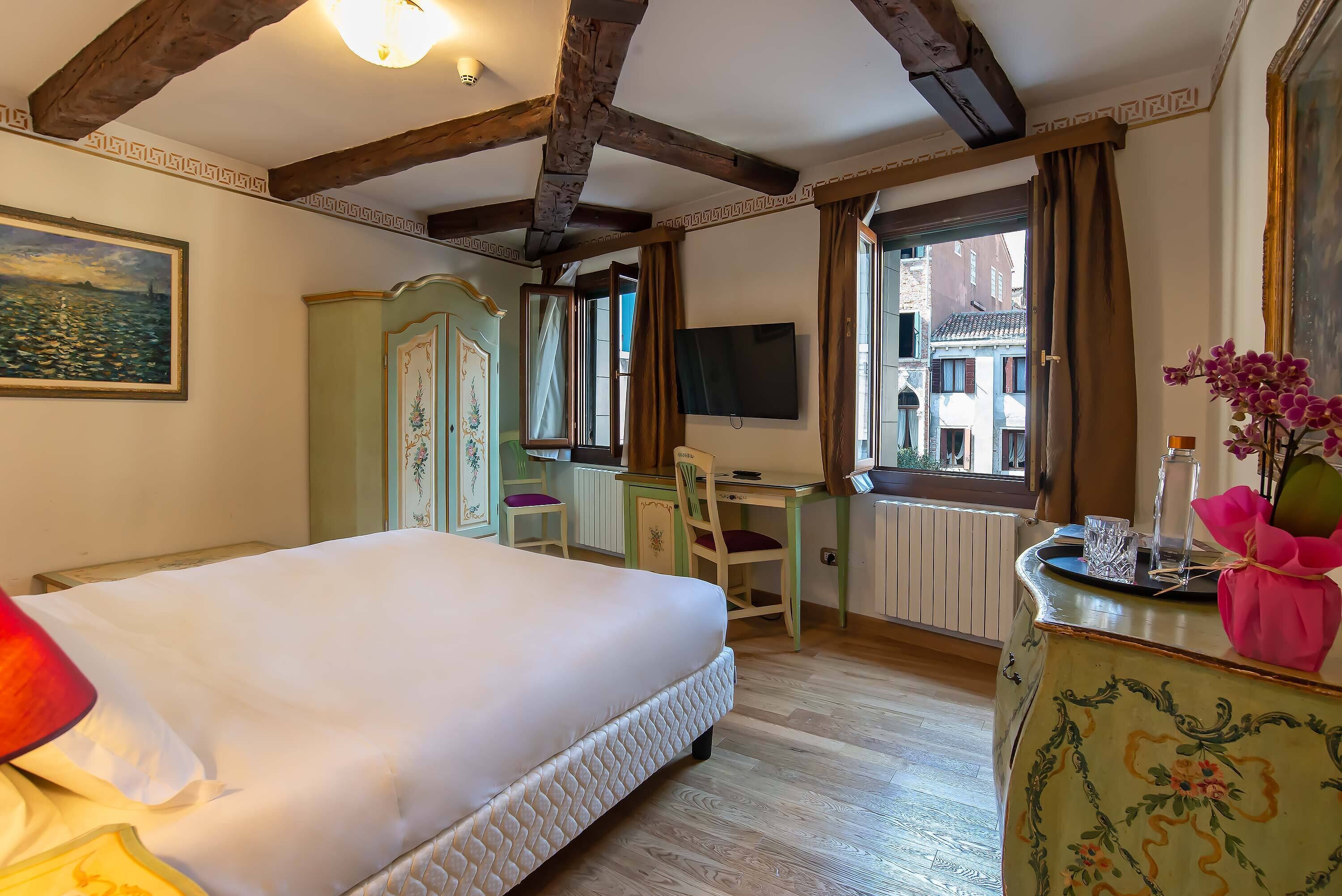 Un dormitorio con una cama grande, un escritorio, una silla, un televisor y una ventana con cortinas.