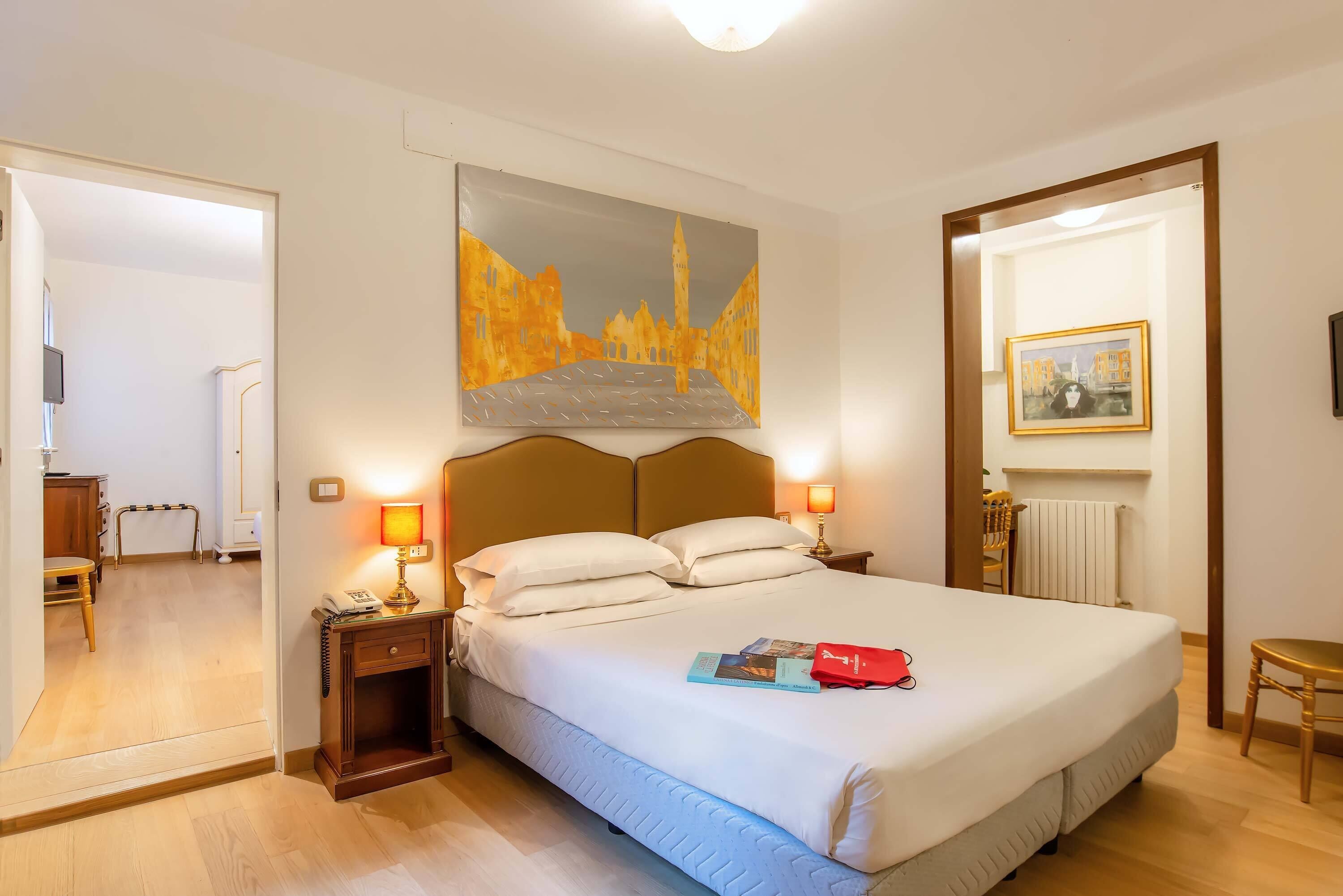 Une chambre d’hôtel avec un grand lit, des lampes de chevet, un tableau au mur et une photographie encadrée au-dessus du lit.