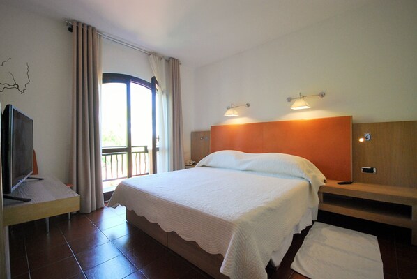 Habitación de hotel con cama, televisor, balcón y cabecero de madera.
