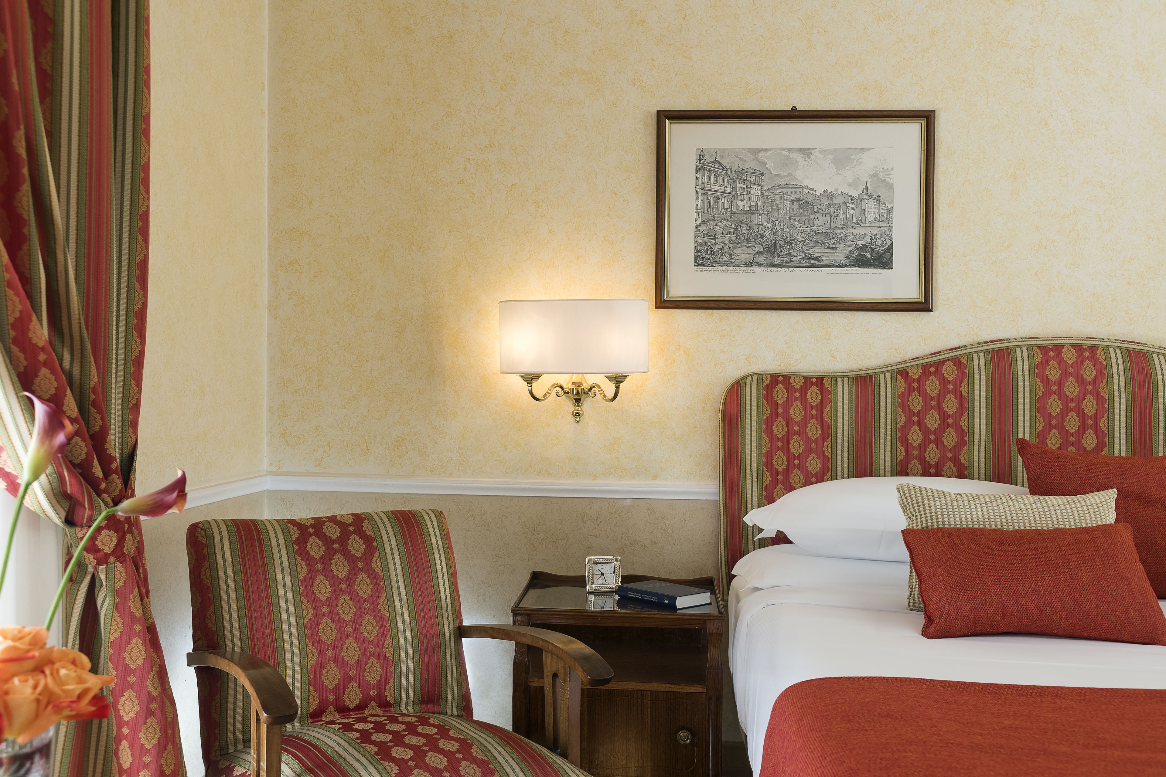 A hotel room with a bed, a nightstand, a chair, a lamp, and a framed picture on the wall.
