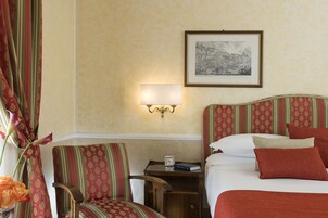 Ein Hotelzimmer mit einem Bett, einem Nachttisch, einem Sessel, einer Lampe und einem gerahmten Bild an der Wand.