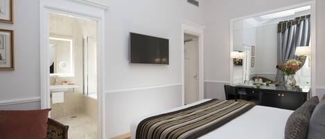 A hotel room with a large bed, a flat-screen TV, a desk with a mirror, and a bathroom visible through an open door.