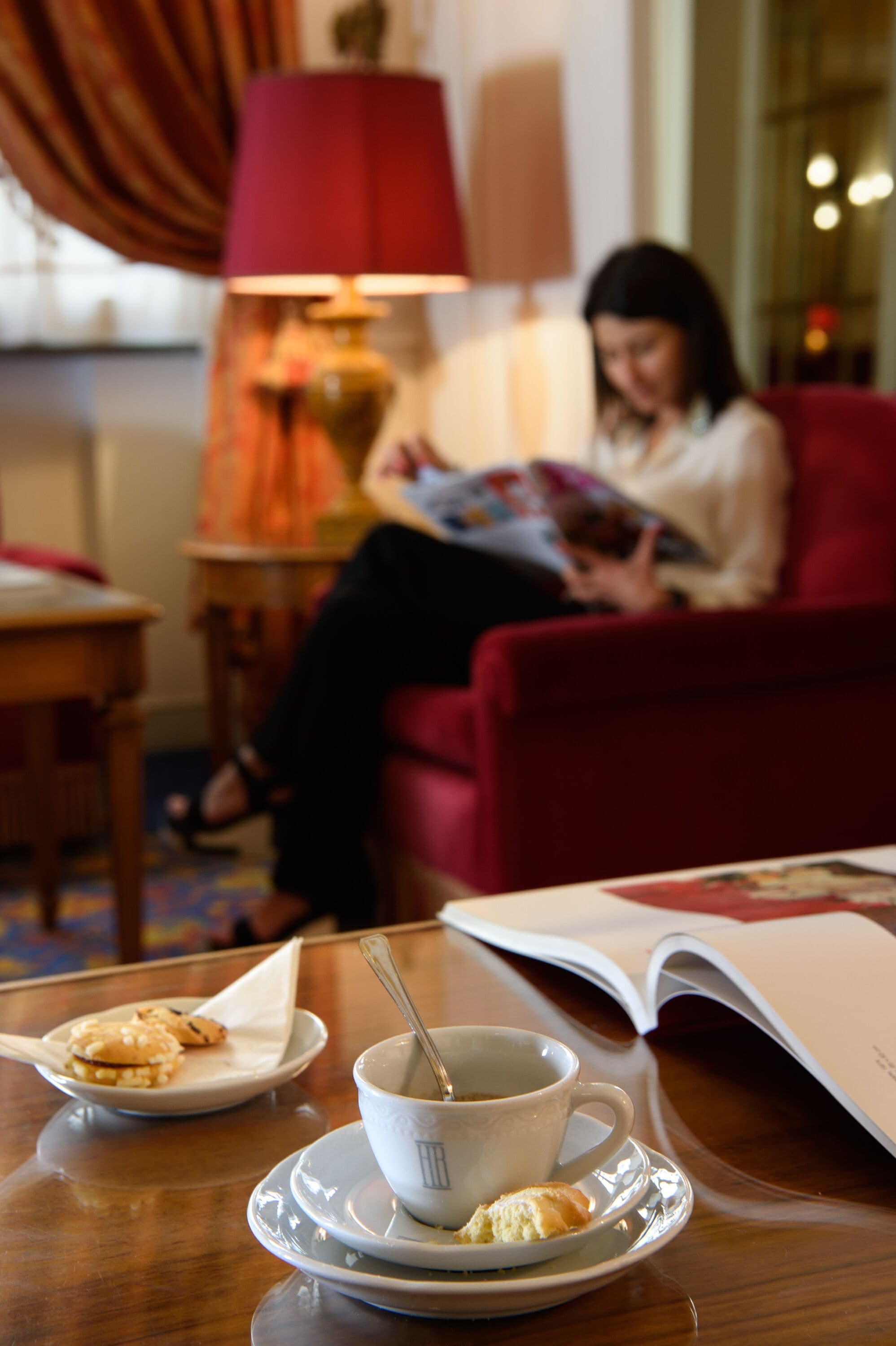 A cozy room with a red sofa, a table with a cup of coffee and biscuits, and a person reading a book.