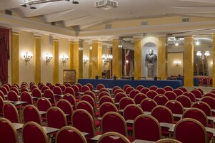 A conference room with rows of red chairs, a stage with a blue table, and a statue in the background.