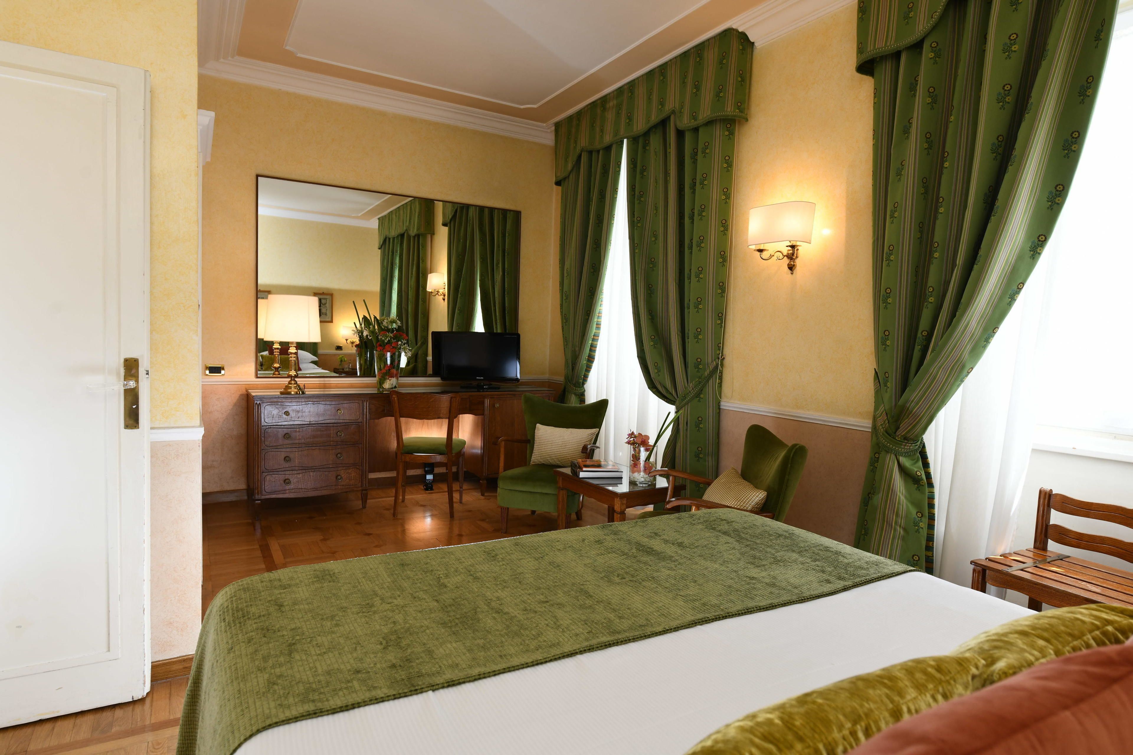 A hotel room with a bed, a desk with a chair, a television, and a mirror.