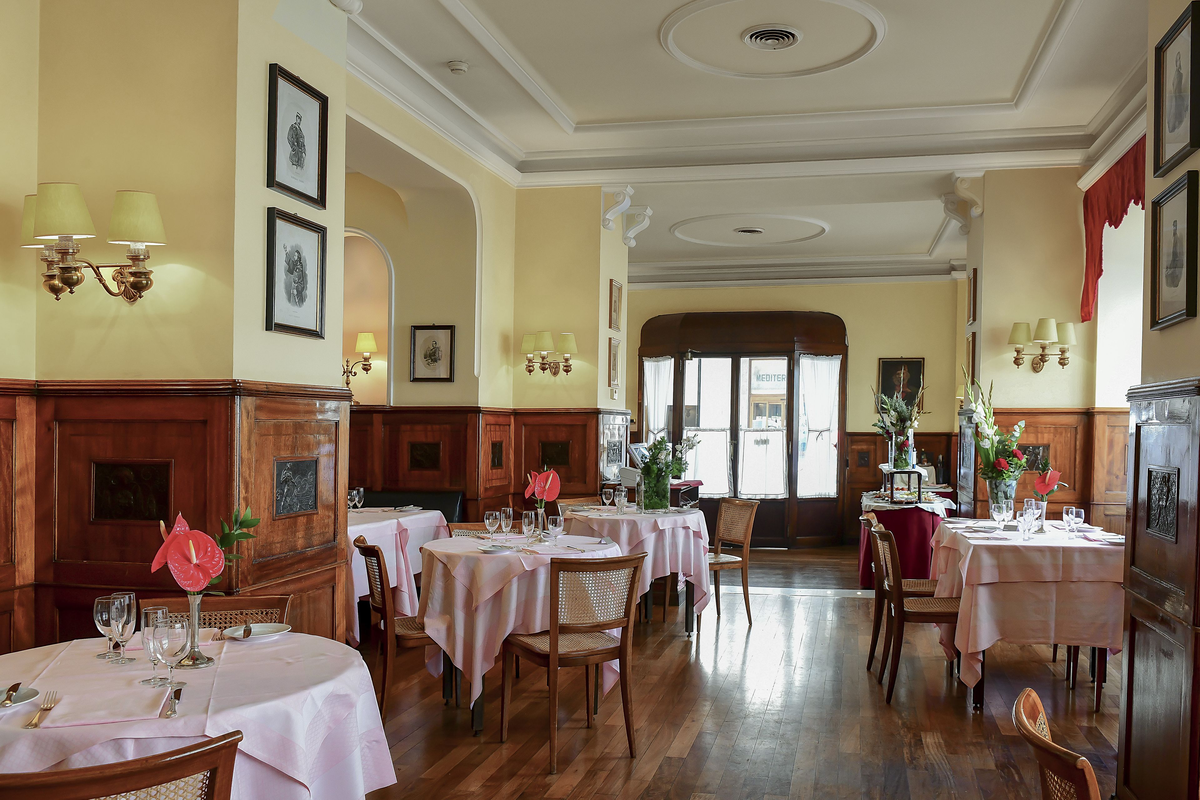 A dining area with multiple tables set for guests, wooden paneling on the walls, and framed artwork on the walls.