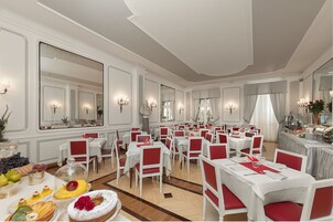 A formal dining room with multiple tables and chairs, large mirrors, and chandeliers.