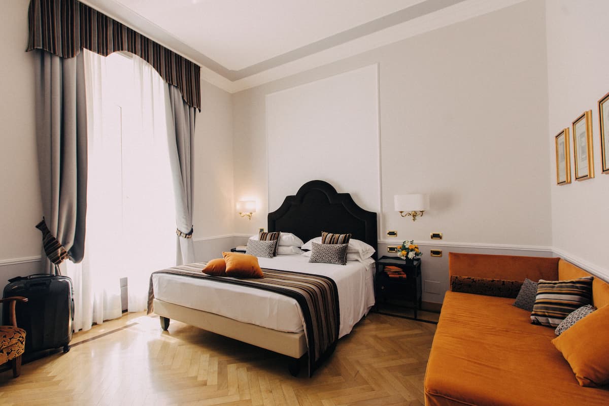 Ein Hotelzimmer mit einem großen Bett, einer Couch, einem Nachttisch und einem Fenster mit Vorhängen.