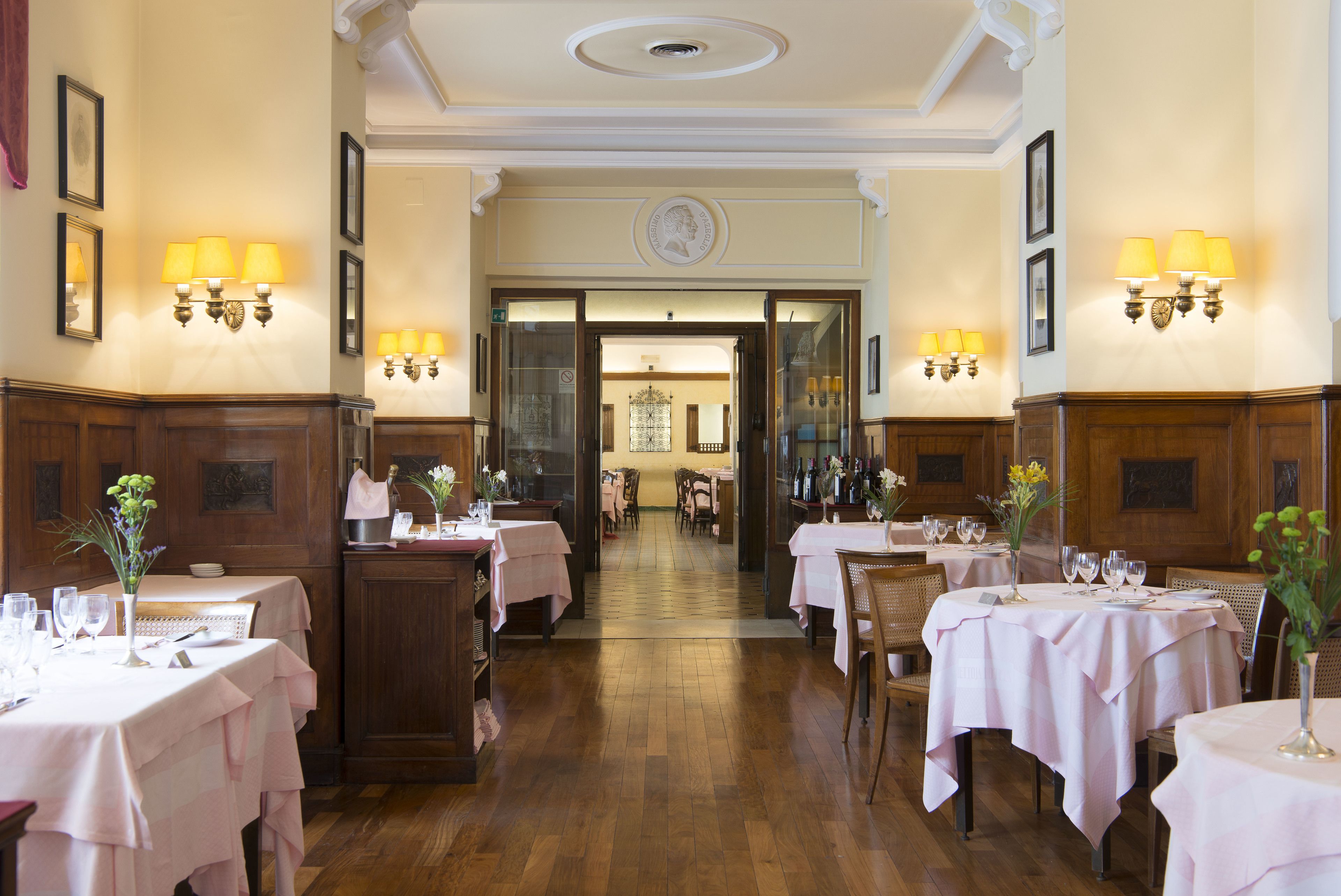 Une salle à manger élégante, avec des tables dressées pour le service, des boiseries et des luminaires fixés au mur.