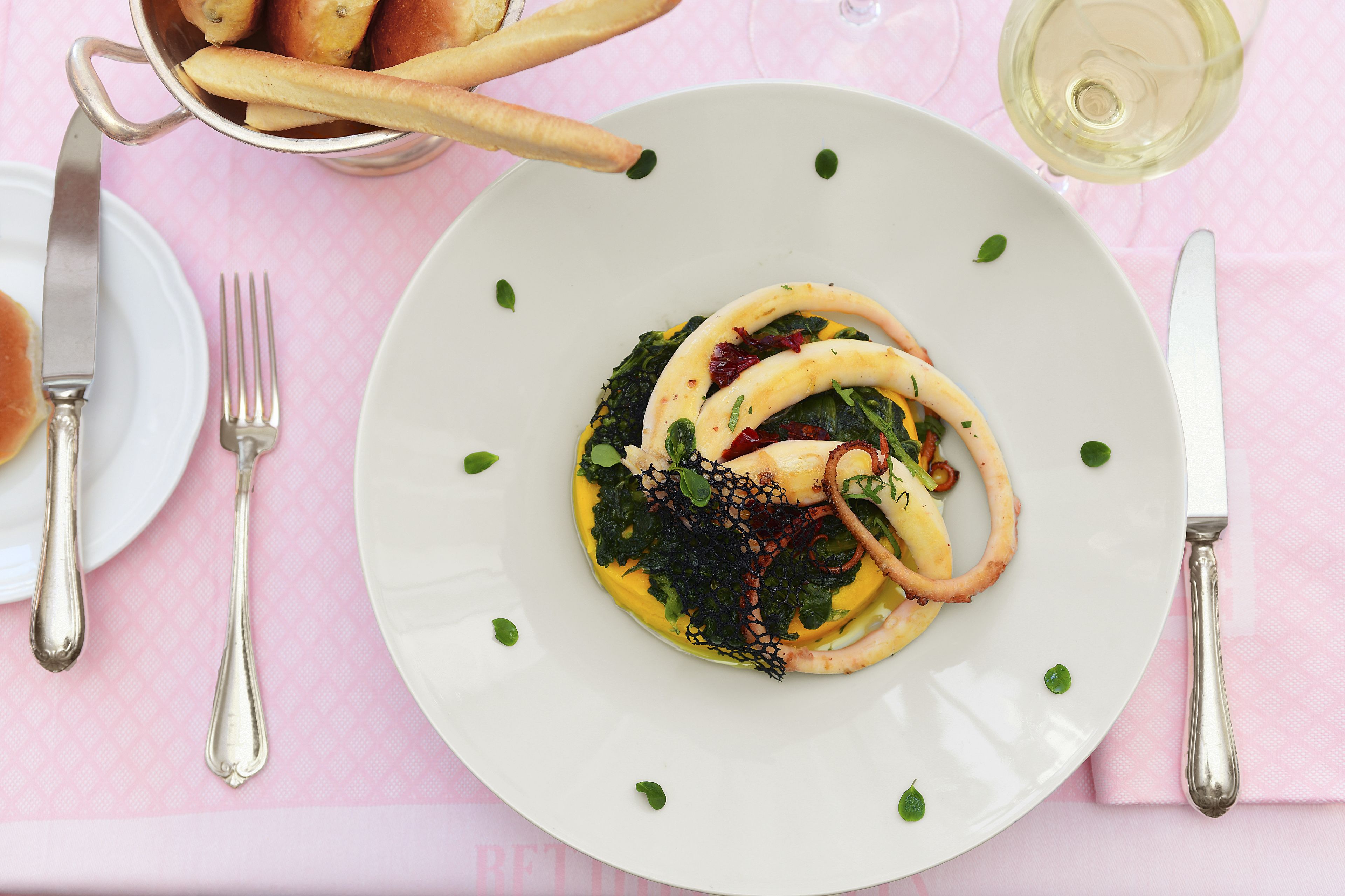 A plate of food with a fork and knife on a pink tablecloth.